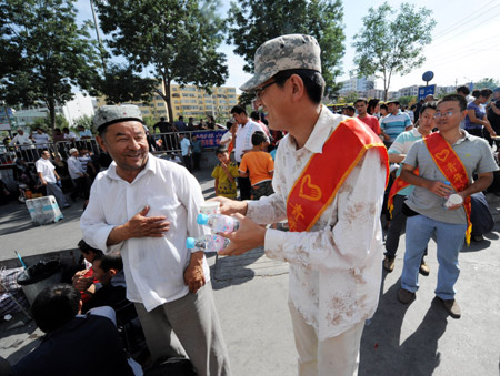 A volunteer sends a cup of water to a passenger at a passenger transport station in Urumqi, capital of northwest China's Xinjiang Uygur Autonomous Region, on July 11, 2009.