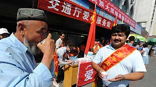 A volunteer sends a cup of water to a passenger at a passenger transport station in Urumqi, capital of northwest China's Xinjiang Uygur Autonomous Region, on July 11, 2009. Several hundred volunteers have gathered at transport stations and hospitals here to provide help since local government began to recruit volunteers on July 10.