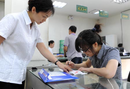 Student of Xinjiang University Tang Juan (R) fills in a form with the help of an employee at the Santunbei Branch of the Urumqi Post Bureau in Urumqi, capital of northwest China&apos;s Xinjiang Uygur Autonomous Region, on July 14, 2009. By now, all the 33 delivering outlets, 69 community outlets and 107 business outlets of the Urumqi Post Bureau have returned to normal work after the deadly riot on July 5. 