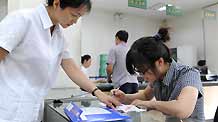 Student of Xinjiang University Tang Juan (R) fills in a form with the help of an employee at the Santunbei Branch of the Urumqi Post Bureau in Urumqi, capital of northwest China's Xinjiang Uygur Autonomous Region, on July 14, 2009.