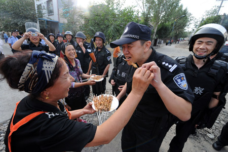 Amyna presents her home-made kabob to members of the special police force on Pingding Hill in Urumqi, capital of northwest China's Xinjiang Uygur Autonomous Region, July 14, 2009. The residents of various ethnic groups living on Pingding hill resumed their peaceful and harmonious life after the deadly July 5 riot, thanks to the peacekeeping police force who managed to maintain ethnic unity and social stability here by helping locals recognize the truth and publicising the ethnic policy with their sincerity. 