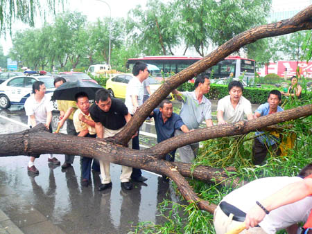 Chinese people help remove a tree broken by strong wind in a heavy rainfall as the traffic is blocked on a road in Beijing, capital of China, on July 22, 2009. A heavy rainfall hit China&apos;s capital city on Wednesday evening.