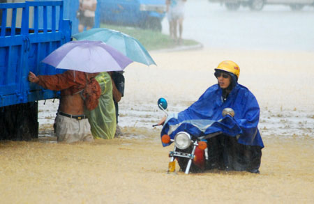 A man pushes his motorcycle past a stranded truck on a flooded street as a heavy rainstorm hits Jiujiang city in east China's Jiangxi Province, on July 29, 2009. Local emergency department employees of the city are on standby to answer emergent calls as some local streets were flooded.