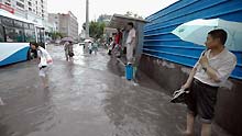 People wait for bus at a flooded section of the Xietu Road in Shanghai, China, on July 30, 2009.