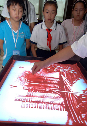 Students watch an artist painting a sand drawing with the theme of environmental protection during a launch ceremony of a project of energy conservation education in Beijing, capital of China, on August 5, 2009.