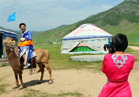 Tourists dressed in Mongolian costumes take photos in front of Mongolian yurts in Horqin Youyi Qianqi, north China's Inner Mongolia Autonomous Region, on August 6, 2009. Since the yurt dwellings of nomadic Mongolians on the grand prairie of Inner Mongolia Autonomous Region attracted more and more tourists from home and abroad, a number of herdsmen living here have invested in the vacation villages or received tourists in their own homes to earn money in recent years. 