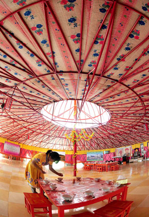 A waitress prepares the dishware set for tourists in a Mongolian yurt in Horqin Youyi Qianqi, north China's Inner Mongolia Autonomous Region, on August 6, 2009. 