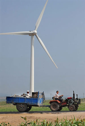 A tractor drives past a white turbine of wind power plants in Hinggan League (or prefecture) of north China's Inner Mongolia Autonomous Region on Aug. 7, 2009. Inner Mongolia, covering 1.18 million square kilometers of land, has boasted more than 3 million kilowatts of wind power, the largest of its kind in China. (Xinhua/Wang Song)