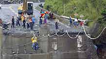 Rescue workers move past a ruined bridge by temporary steel ropes for relief work on the road to Xinkai village in Kaohsiung of Taiwan, on August 12, 2009. The village was hit by debris flow caused by typhoon Morakot, which might result in serious casualties.
