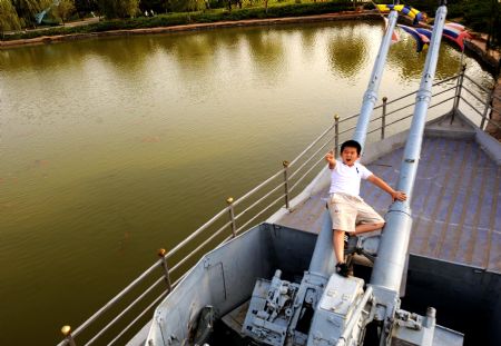 A boy plays on a gunboat displaying at the Weapon Square in Baotou of north China's Inner Mongolia Autonomous Region, on August 19, 2009.