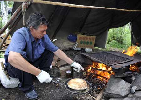  A Rong, a local Owenke used to make his living by hunting, displays a kind of traditional cooking in the Forest Museum in Genhe City of north China