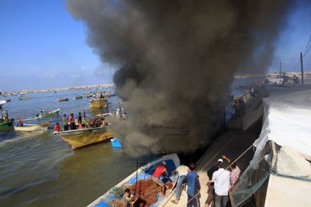 Palestinian fishermen try to put out fire on a boat at the Gaza city port after being hit by an Israeli shell, Aug. 31, 2009. (Xinhua/Mahmud Nassar)