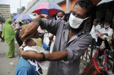 A street vendor helps a boy wear a protective mask in Dhaka, capital of Bangladesh, September 3, 2009. The total number of people infected by A/H1N1 flu in Bangladesh has so far reached 275, as 16 more new cases were detected on Thursday.