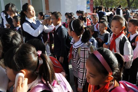 A teacher measures body temperature for students at a primary school in Urumqi, capital of northwest China's Xinjiang Uygur Autonomous Region, on September 14, 2009.