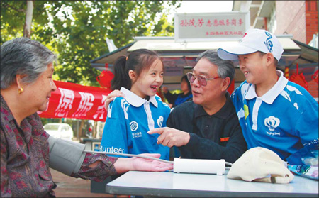 Volunteer Sun Maofang (2nd, R), 66, show young volunteers how to use a blood pressure monitor in Beijing Sunday. 