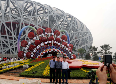 Tourists pose for photos beside a huge parterre in front of the National Stadium or 'Bird's Nest' in Beijing, capital of China, September 24, 2009. The Olympic Park in which the Bird's Nest is located has been decorated to celebrate the 60th anniversary of the founding of the People's Republic of China which falls on October 1. 