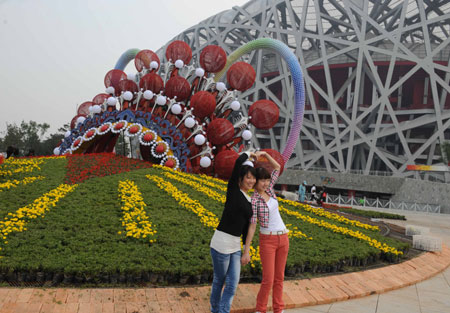 Tourists pose for photos beside a huge parterre in front of the National Stadium or 'Bird's Nest' in Beijing, capital of China, September 24, 2009. The Olympic Park in which the Bird's Nest is located has been decorated to celebrate the 60th anniversary of the founding of the People's Republic of China which falls on October 1. 