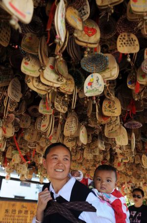 A local woman in traditional dress with a child on her back walks under windbells in Lijiang, southwest China's Yunnan Province, September 29, 2009. 