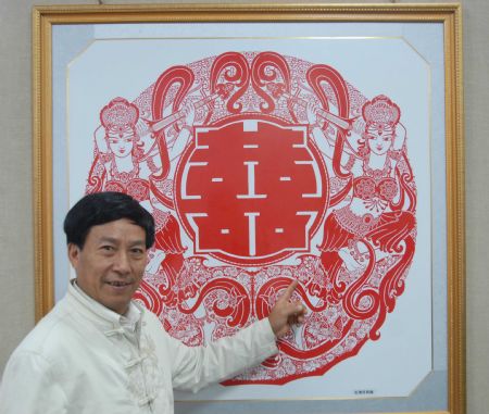 Zhang Zhuquan, a folk artist of paper-cutting of Tujia ethnic group, presents his elaborate paper-cutting work of double happiness, at the exhibition of his personal paper-cutting artwork, where some 60 variously-designed double happiness paper-cutting and paper-carving artworks were on display at the Guiyang Art Gallery, in Guiyang, southwest China's Guizhou Province, October 17, 2009. 