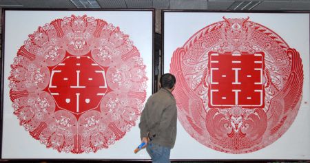 A visitor watches the paper-cutting artwork of double happiness by Zhang Zhuquan, a folk artist of paper-cutting of Tujia ethnic group, at the exhibition of Zhang Zhuquan personal paper-cutting artwork, where some 60 variously-designed double happiness paper-cutting and paper-carving artworks were on display at the Guiyang Art Gallery, in Guiyang, southwest China's Guizhou Province, October 17, 2009. 