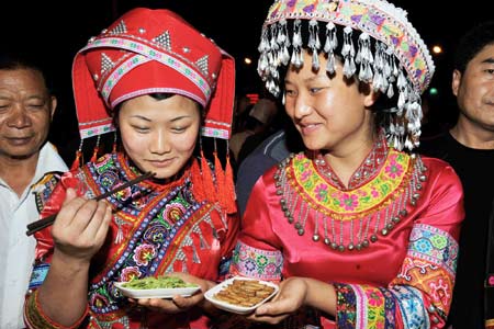 Two women in florid ethnic costumes relish the savour of dainty snacks at the Folklore Food Festival, which lays emphasis on inheritance and carrying forward the characteristic culinary culture of indigenous ethnic minorities, tapping affluent cuisine resources and attach great importance for better preservation, in Wenshan County, Wenshan Zhuang and Miao Autonomous Prefecture, southwest China's Yunnan Province, October 20, 2009.