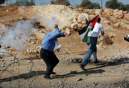 Palestinian demonstrators run to avoid tear gas fired by Israeli troops during a demonstration against Israel's construction of a separation barrier in the West Bank village of Bilin near Ramallah, on October 23, 2009. 