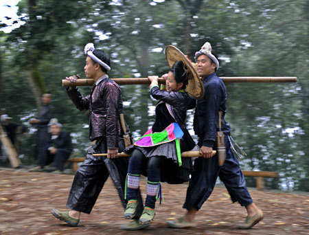 Two young men take a bride with the shoulder pole during a folk show of local villagers of Miao ethnic group, as local villagers of Miao ethnic group gather for a song and dance rendezvous in celebration of this autumn bumper harvest as a result of seasonable weather with gentle breeze and timely rainfalls, in Basha Village, Congjiang County, southwest China&apos;s Guizhou Province, October 24, 2009. 