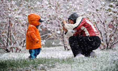 A mother takes pictures of her child on a snow-covered lawn in Beijing November 1, 2009.