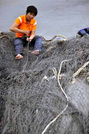 A Fisherman repairs fishing net in a port in Haikou, capital of south China's Hainan Province, November 2, 2009.