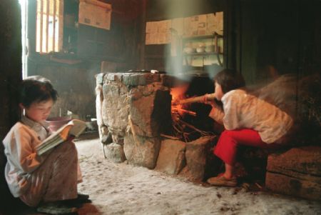 Zheng Meihua (R) cooks supper while her sister Zheng Meitao reads her textbook after school in Taishun County, Zhejiang Province in this photo taken in April, 1994. The sisters went back to school with the help of Hope Project after suffering the death of their parents.