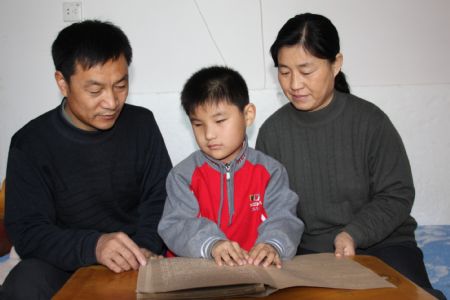 Liu Hao, an eight-year-old blind boy of a worker's family, reads out to his parents by feeling the Braille, in Chifeng City, north China's Inner Mongolia Autonomous Region, November 3, 2009. 