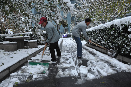 People clean up snow on a road in the Yicuiyuan community in Beijing, capital of China, November 10, 2009. Beijing witnessed the second snowfall this winter on November 10.