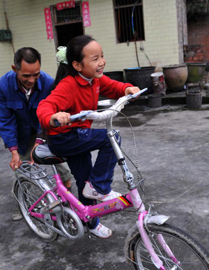 Gao Yaqian, an 8-year-old pupil of the Central Primary School of Lirang Town, learns riding bicycle at home, in Liangping County, southwest China's Chongqing municipality, October 30, 2009.