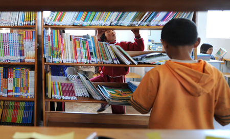 Several students skim through books on bookshelves inside the reading room on the campus of the Orphanage School for Ethnic Minorities in Lijiang, southwest China's Yunnan Province, October 27, 2009.