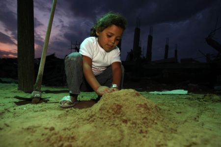 Mona Khader plays the game of building houses at the sand pile near the tent, in which she lives in the Gaza Strip, on October 29, 2009. 