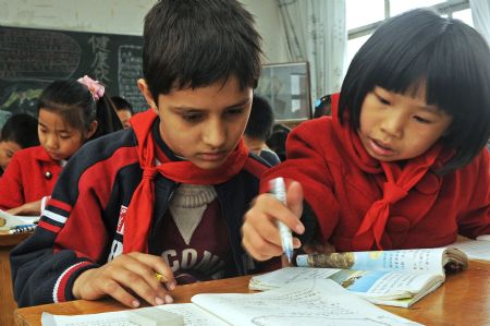 Classmate Zheng Chenxin (R) helps Sanlong in Chinese-language class in Wu'ai Primary School in Yiwu City, east China's Zhejiang Province, November 13, 2009.