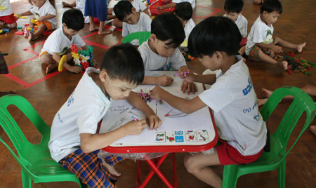 Three children draw pictures as others play games at the Htauk Kyant Orphanage in Yangon, Myanmar, on November 18, 2009. 