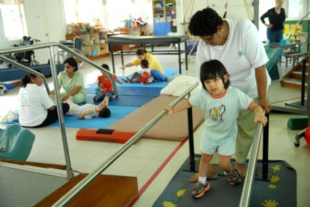 A trainer helps four-year-old Mia, who is hearing-impaired, train her walking skills at Tasputra in Kuala Lumpur, Malaysia, on Nov. 20, 2009. Tasputra is a non-profitable charity center aiming to care and train special children. There are 52 children of different ethnic groups being trained here to achieve the goal of self-independence. (Xinhua/Chong Voon Chung)