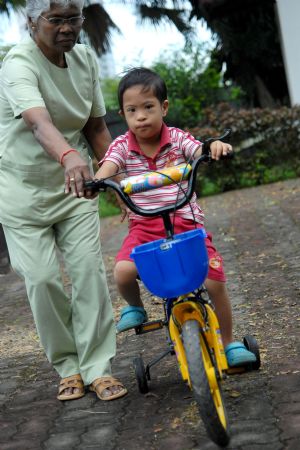 A trainer helps a special child ride a bicycle at Tasputra in Kuala Lumpur, Malaysia, on Nov. 20, 2009.(Xinhua/Chong Voon Chung)