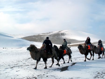Tourists on camel back pass the snow covered Mingshashan in Dunhuang, northwest China&apos;s Gansu Province December 14, 2009. 