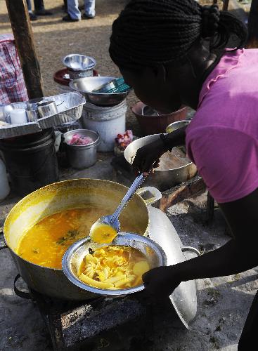A woman fills a bowl with food at a temporary settlement for quake victims outside the presidential palace in Port-au-Princes, capital of Haiti, January 31, 2010.
