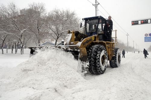 People drive a bulldozer to clear snow on the road in Kuitun City, northwest China's Xinjiang Uygur Autonomous Region, Feb. 23, 2010. 