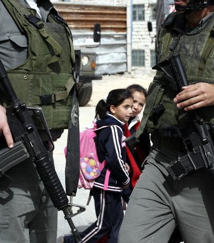 Palestinian school girls walk past Israeli soldiers during clashes in the West Bank city of Hebron, Feb. 24, 2010.