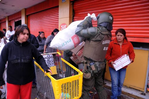 A policeman tries to keep order as people run away with looted merchandise in the quake-devastated Concepcion, Chile, March 1, 2010. 