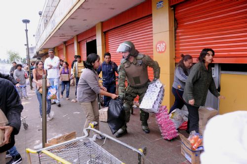 A policeman tries to keep order as people run away with looted merchandise in the quake-devastated Concepcion, Chile, March 1, 2010.