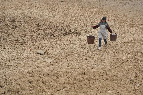 A villager carries buckets to fetch water on a dried pond in Panxian, southwest China's Guizhou Province, on March 10, 2010. 