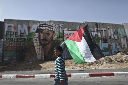 A Palestinian boy waves a flag as he walks past a section of Israeli controversial separation barrier during a demonstration against Israeli closure in Qalandiya checkpoint near Jerusalem city on March 13, 2010.