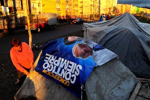 A woman covers her tent with a plastic poster in Conception, Chile, on March 17, 2010.