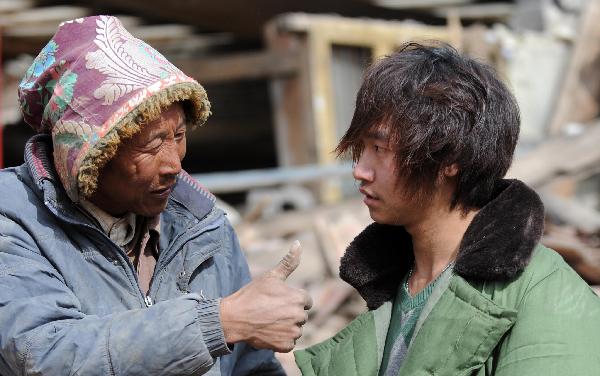 A Tibten resident praises Yang Yang (R), a 23-year-old young man who saved seven lives from the quake debris, in front of the house that witnessed his heroism in Gyegu, northwest China's Qinghai Province, April 17, 2010. 