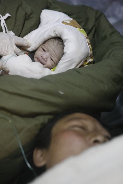 A newborn baby is seen with her mother at a makeshift shelter in Gyegu Town, Yushu County, northwest China's Qinghai Province, on April 17, 2010.